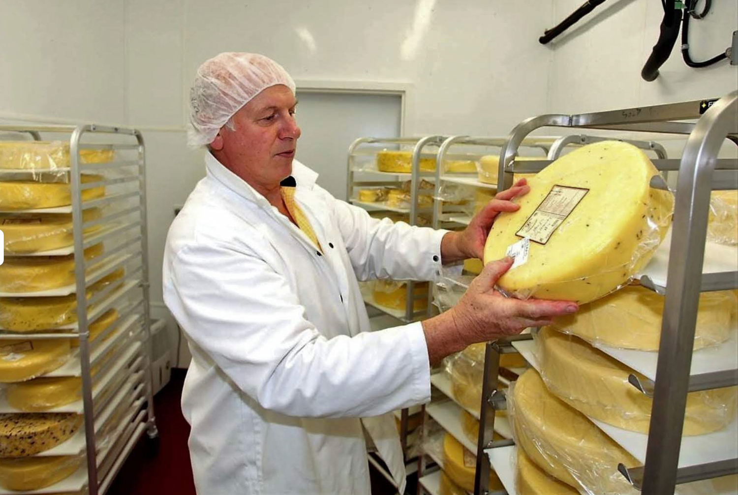 Frazer Hunter of Knoydart holding a large wheel of cheese in the cheese aging room